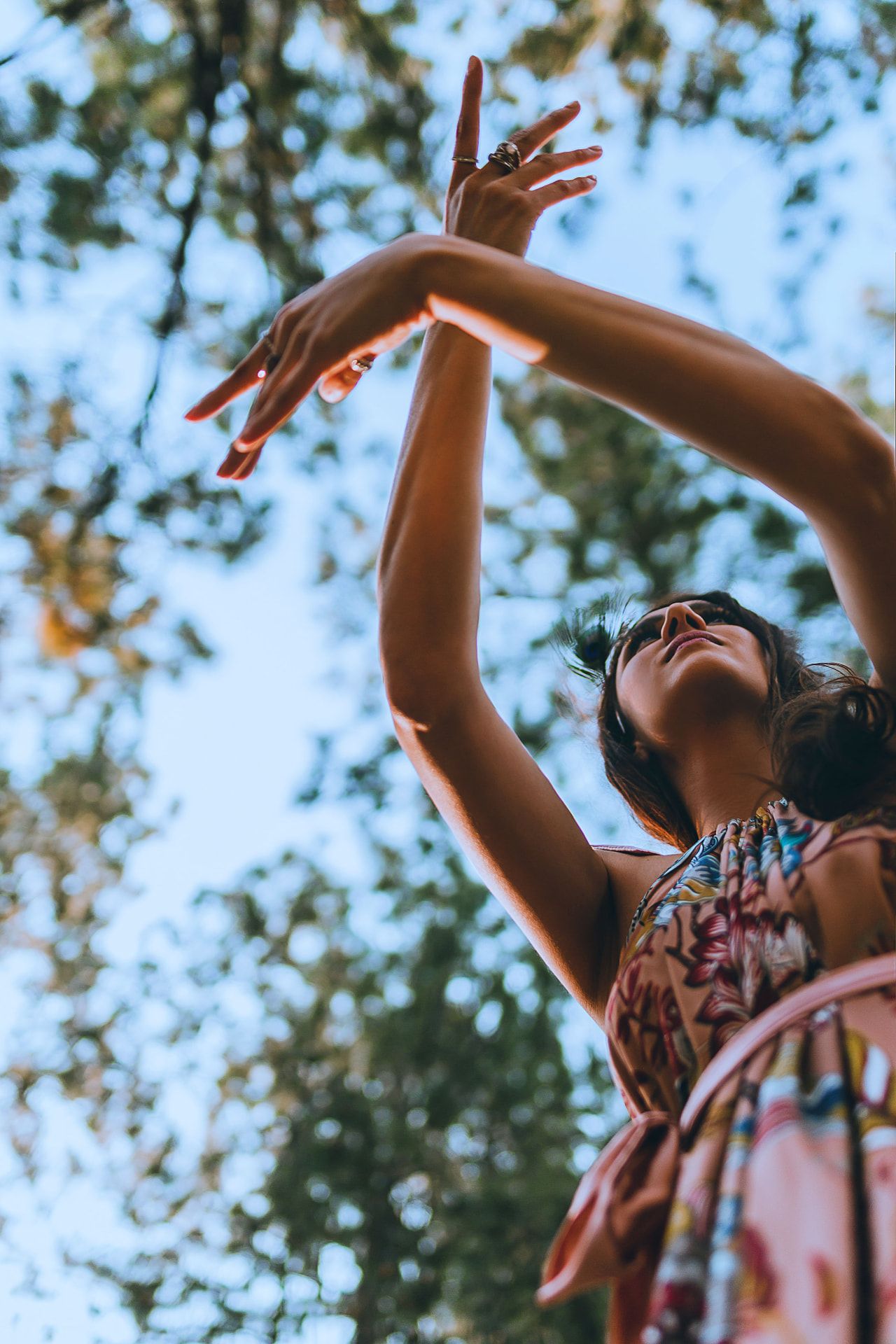Noa reaching skyward through pine branches, hands crossed in a gesture of offering