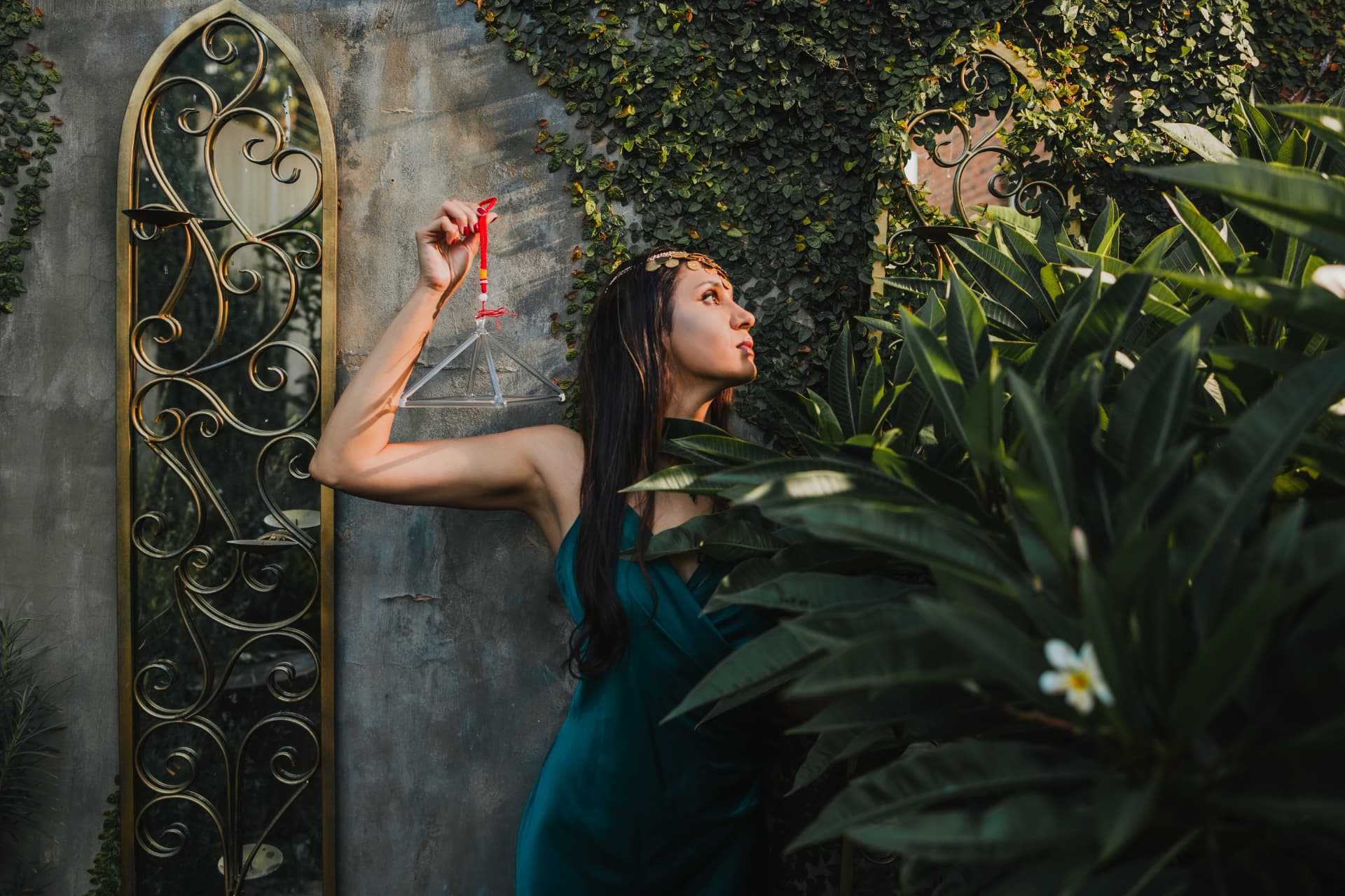 Noa in an emerald dress sounding a ceremonial triangle in a lush garden