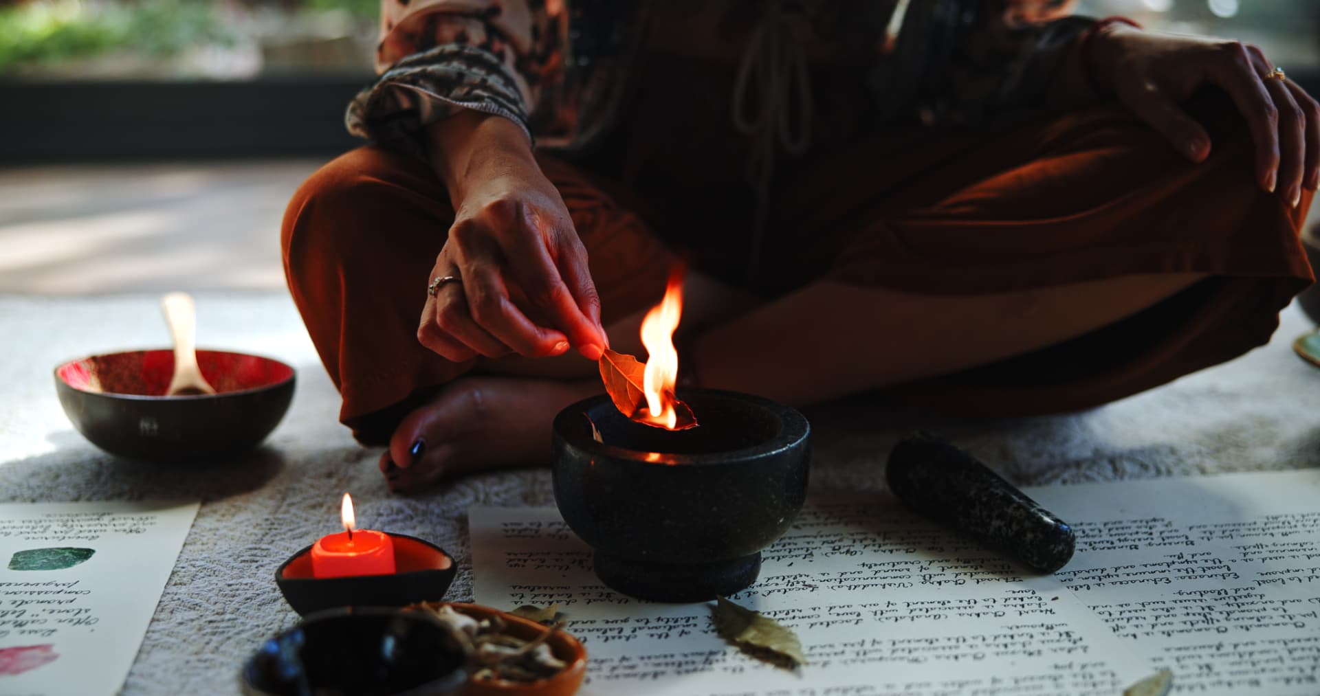 Noa lighting a bay leaf over a stone mortar beside candlelight