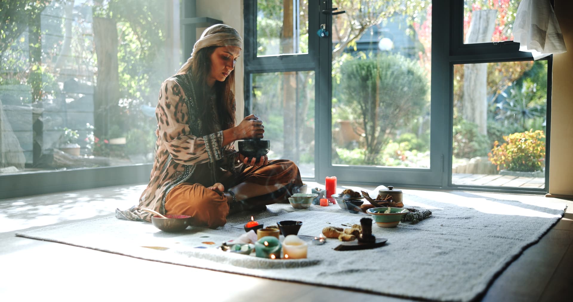 Noa seated on a ceremonial cloth grinding herbs in a stone bowl