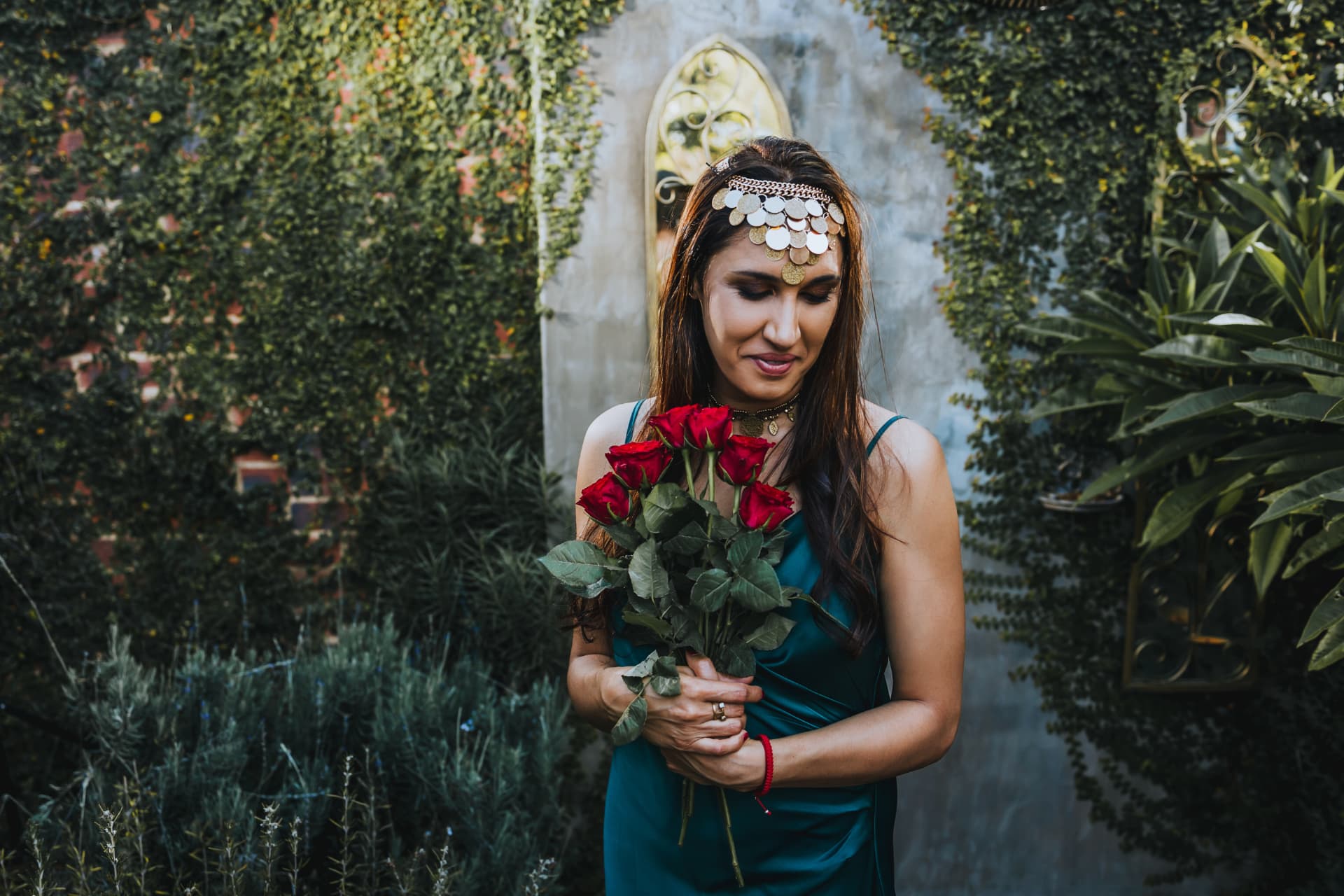 Noa holding a bouquet of red roses against an ivy-covered garden wall