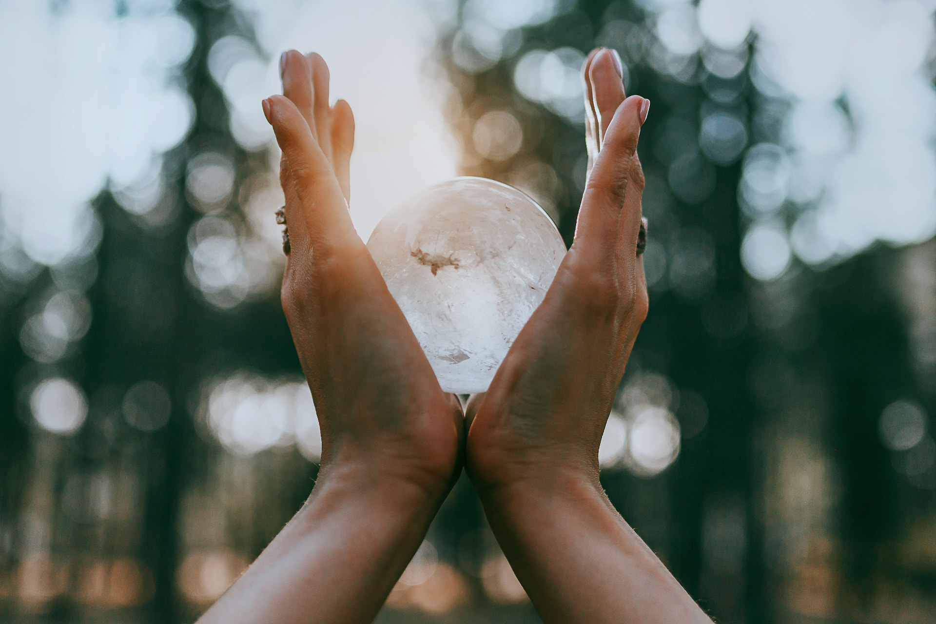 Hands cradling a glowing clear quartz sphere in a forest at golden hour