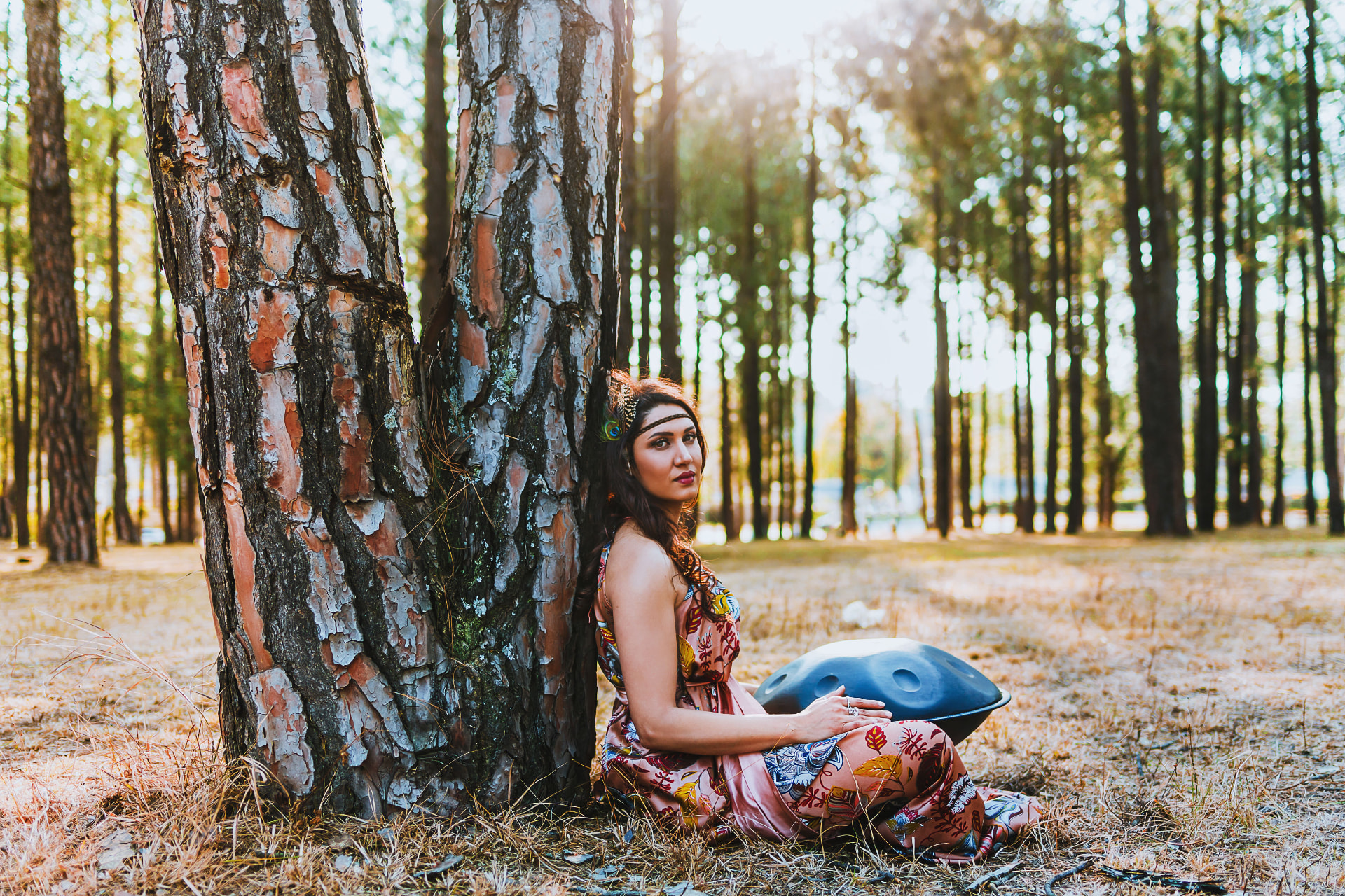 Noa leaning against a tree in a sunlit forest with a handpan, resting into stillness