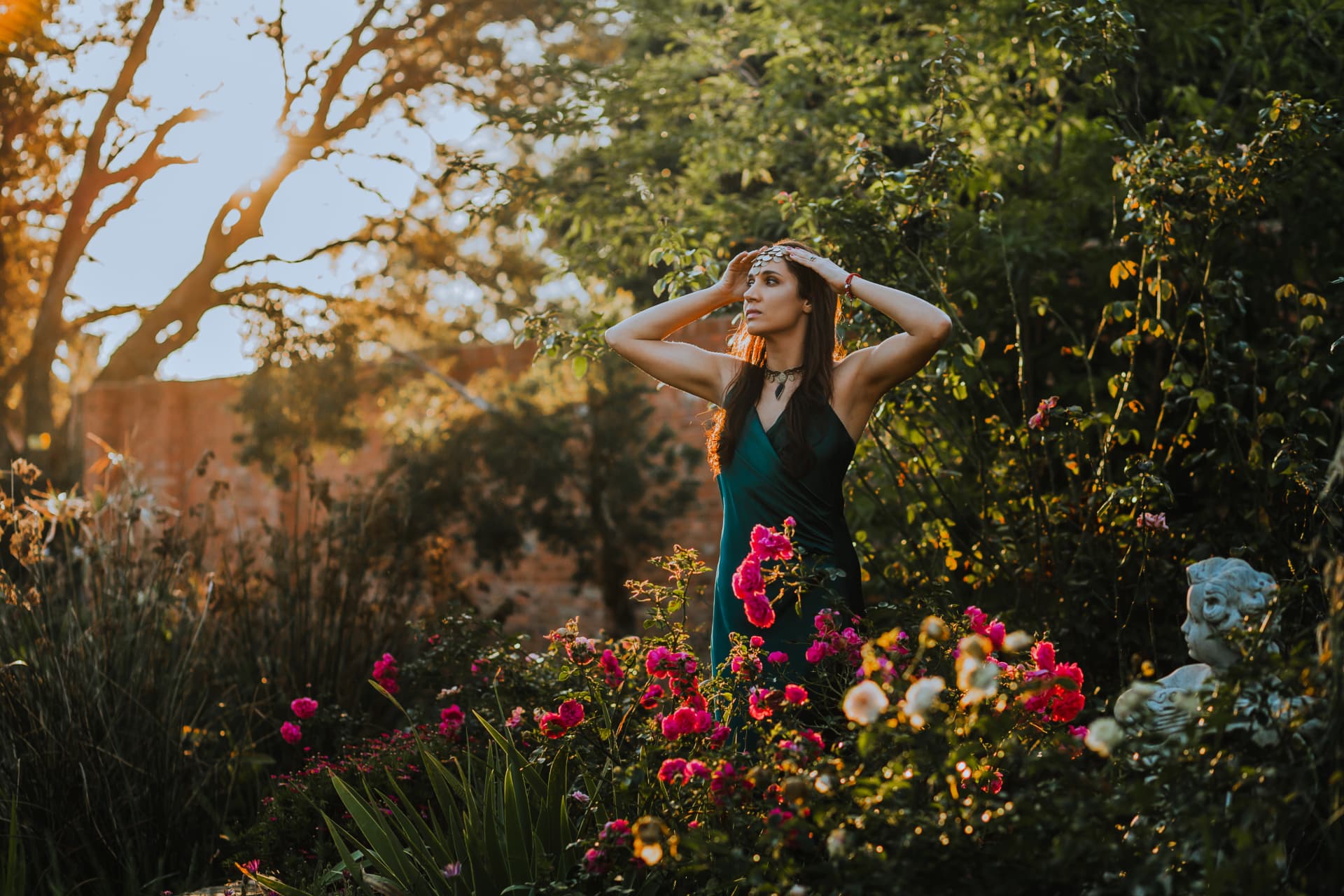 Noa standing among blooming roses at sunset in an emerald silk dress