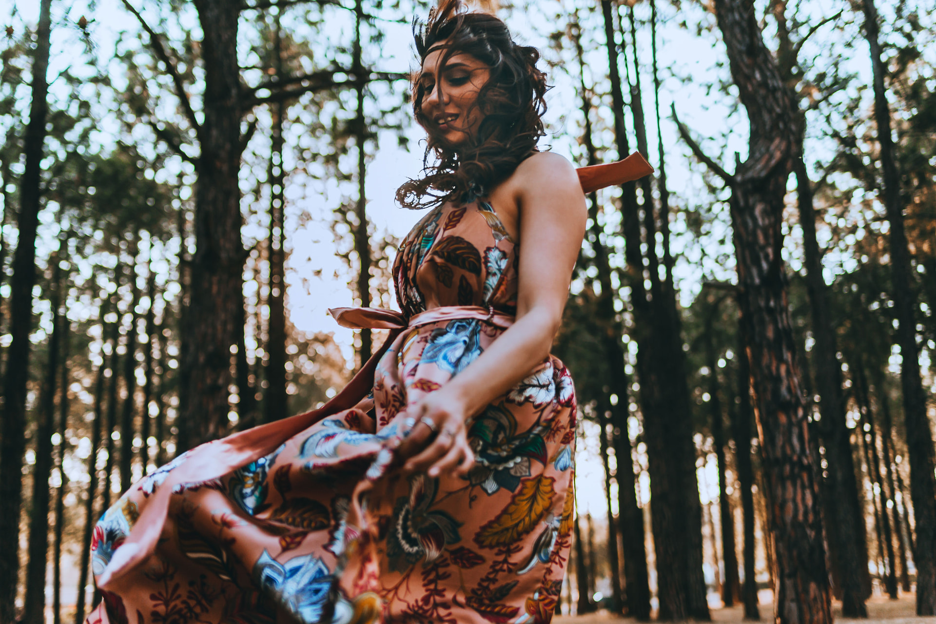 Noa turning in a sunlit pine forest, her floral dress sweeping around her